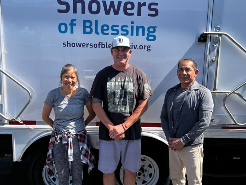 Three volunteers in front of the Shower of Blessings truck